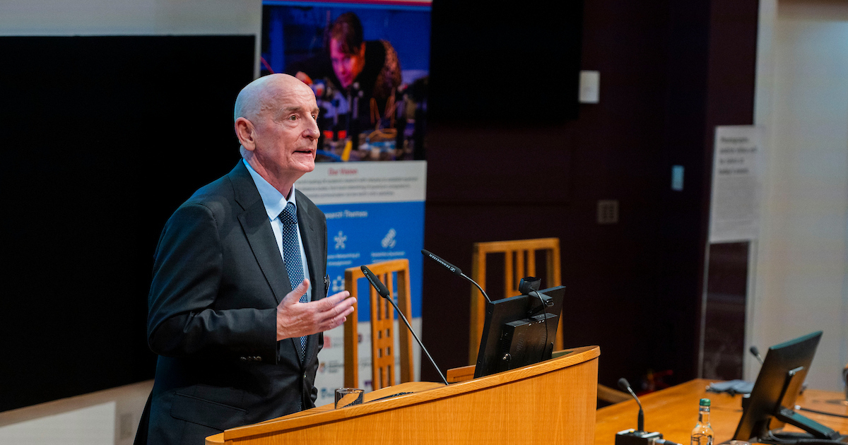 Image showing the Hub Director, Professor Gerald Buller (a white, middle-aged man) addressing the audience in a lecture theatre at the Hub launch event
