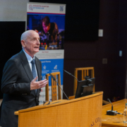 Image showing the Hub Director, Professor Gerald Buller (a white, middle-aged man) addressing the audience in a lecture theatre at the Hub launch event