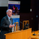 Image showing the Hub Director, Professor Gerald Buller (a white, middle-aged man) addressing the audience in a lecture theatre at the Hub launch event