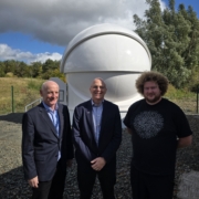Photograph showing three white men in front of a optical ground station facility.