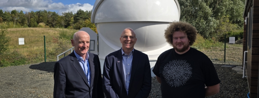 Photograph showing three white men in front of a optical ground station facility.